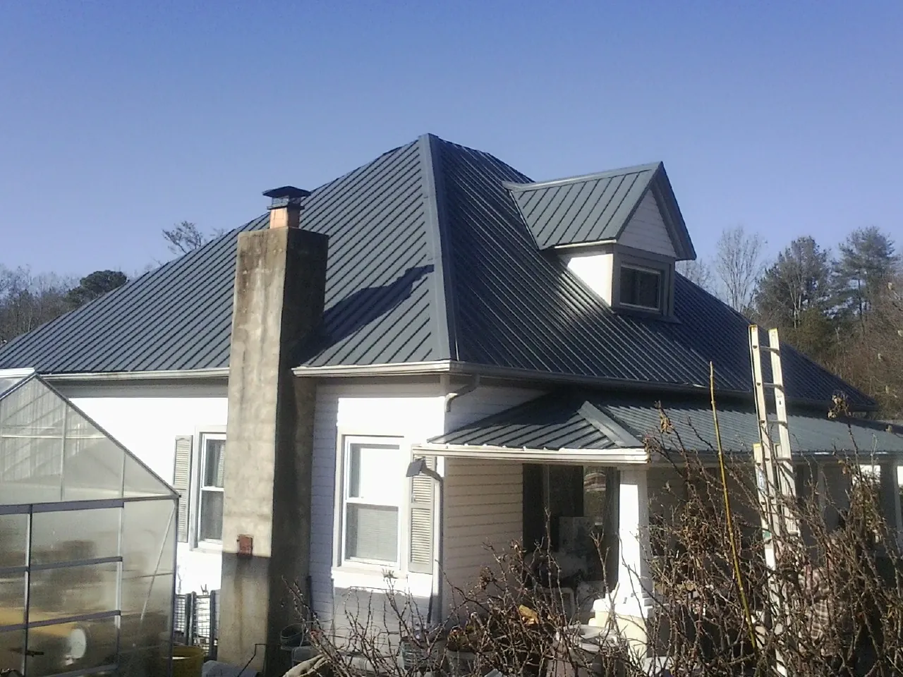 Dark blue standing seam metal roof on a white farmhouse with dormer — Slate & Tile Roof Repair by Roofing Brothers in New Springfield