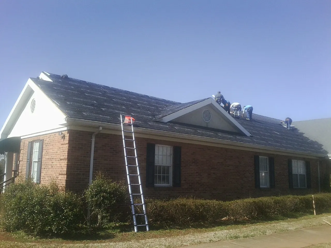 Crew tearing shingles off a brick ranch roof with a ladder set — Metal Roof Repair work by our crew in New Springfield