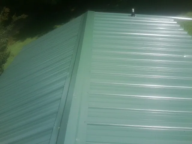 New green metal panels meeting at the ridge of a roof — Flat Roof Repair work by our crew in New Springfield