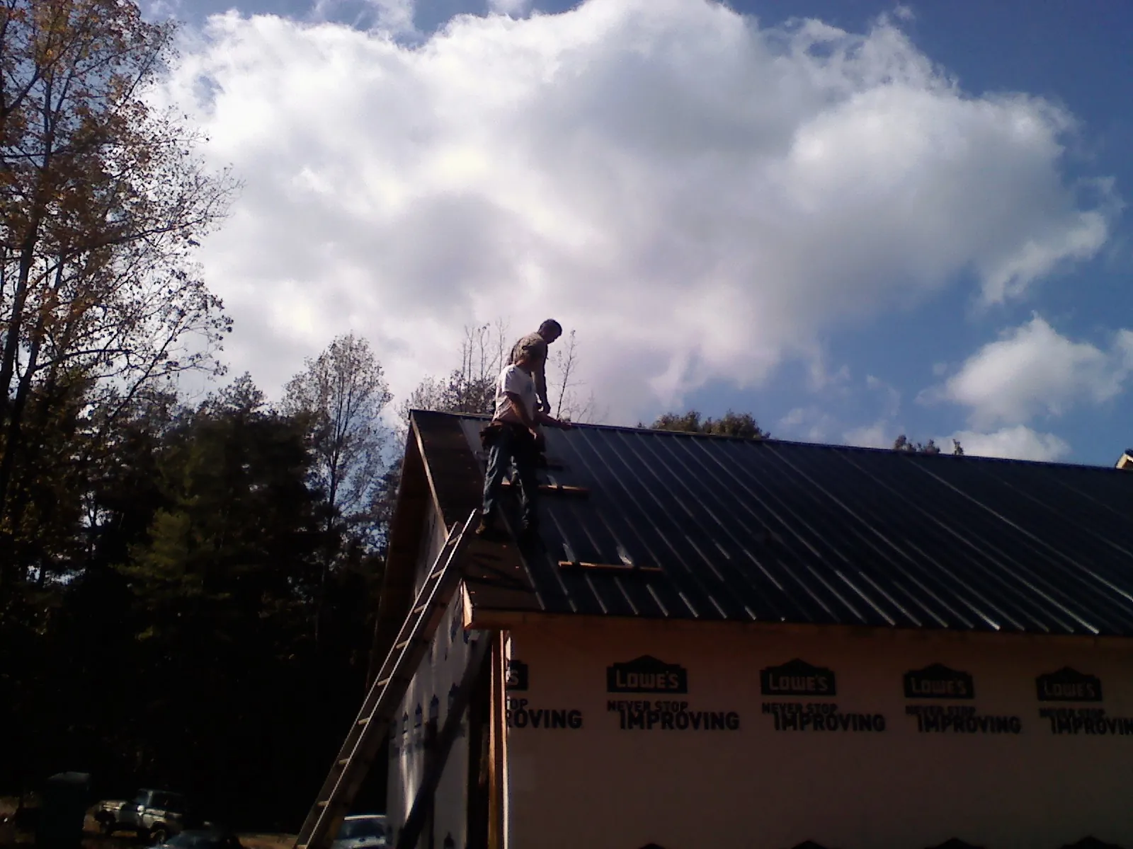 Roofer fastening dark metal panels high against a cloudy sky, from a Roof Inspection job in New Springfield