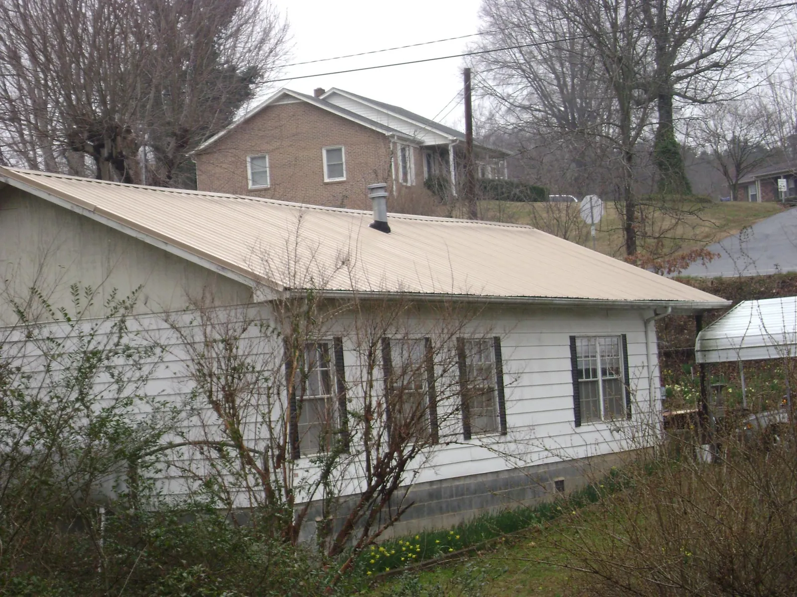 Tan metal roof on a white sided house set into a hillside — Commercial Roofing by Roofing Brothers in New Springfield